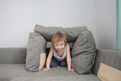 Kid toddler builds house from pillows on sofa in living room, lifestyle and games in real interior