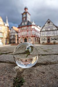 Close-up of crystal ball on glass against building in city