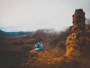 Rear view of person sitting on rock against sky