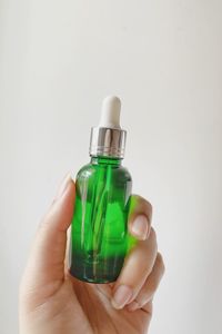 Cropped hand holding bottle against white background