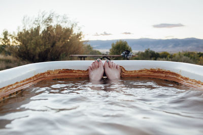 Low section of woman in bathtub against sky