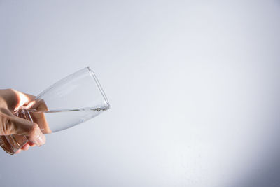 Cropped hand pouring water from glass against gray background