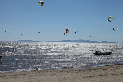 People flying over beach against clear sky