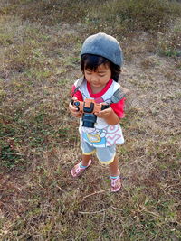 High angle view of girl holding toy camera standing outdoors