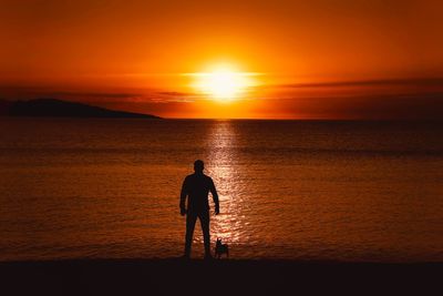 Silhouette woman standing at beach against sky during sunset