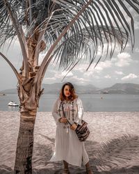 Portrait of woman standing by palm tree against sea