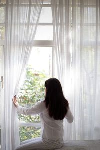 Rear view of woman looking through window