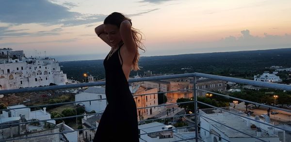 Side view of woman standing on building terrace during sunset