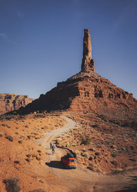 An orange car is driving through the valley of gods, utah