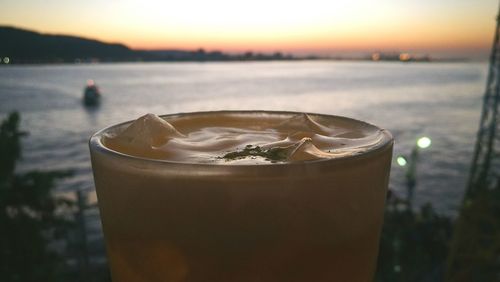 Close-up of coffee against sea during sunset