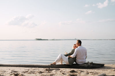 Rear view of couple sitting on shore against sky