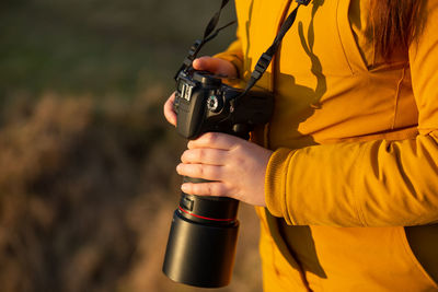 Midsection of woman holding camera standing outdoors