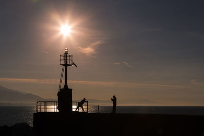 Silhouette built structure by sea against sky during sunset