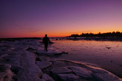 Silhouette man standing on rock at beach against sky during sunset