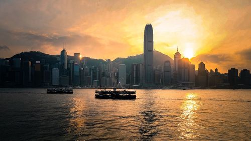 Ferries sailing at victoria harbour by modern buildings against sky during sunset