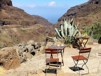 Chairs and cactus on mountain against sky