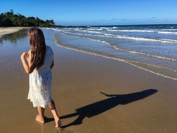 Rear view of woman standing on beach against sky