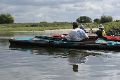 People sitting on boat in lake against sky