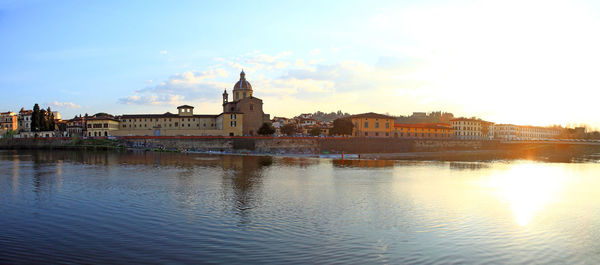 Buildings at waterfront against cloudy sky