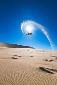 Scenic view of desert against bright sun in clear blue sky