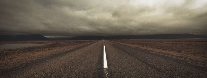 Road passing through landscape against cloudy sky