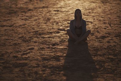 Woman sitting on ground at sunset