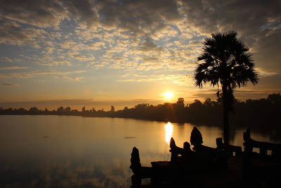 Silhouette people sitting by palm trees against sky during sunset