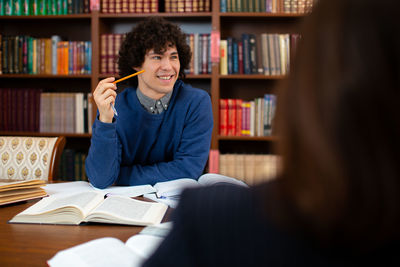 Man looking away while gesturing over book by woman at table