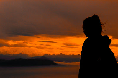 Silhouette woman standing by sea against orange sky