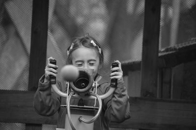 Portrait of girl holding camera while standing by fence