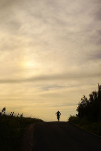 Silhouette man on road against sky during sunset