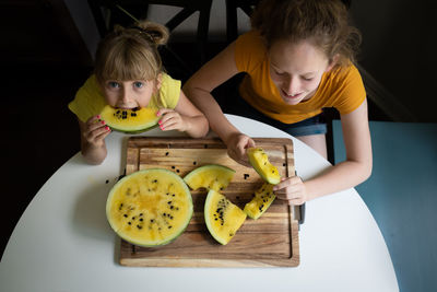 High angle view of sisters eating melon at home