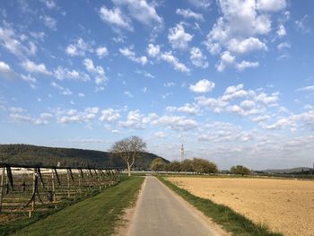 Empty road amidst field against sky