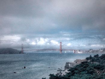 Suspension bridge over sea against cloudy sky