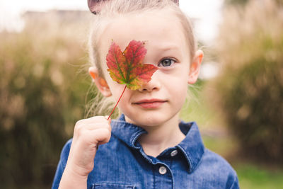 Portrait of girl covering face with maple leaf outdoors