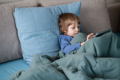 Boy laying in bed and communicating with grandma via video chat using laptop during coronavirus