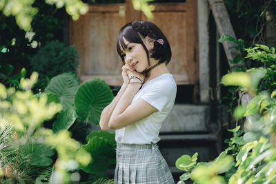 Side view of young woman standing against plants