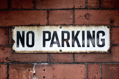 Close-up of no parking sign on brick wall