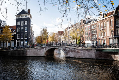 Bridge over river by buildings in city against sky