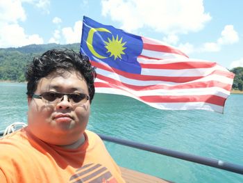 Portrait of overweight man wearing sunglasses against malaysian flag in sailboat