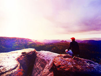 Man sitting on rock looking at mountain against sky