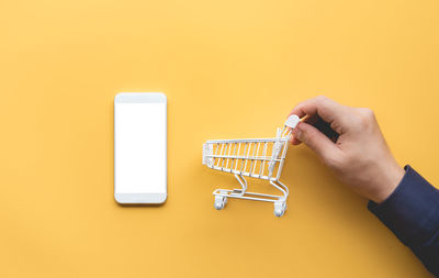 Close-up of hand holding smart phone against yellow background