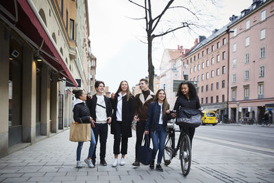 Smiling male and female teenage friends walking on sidewalk in city