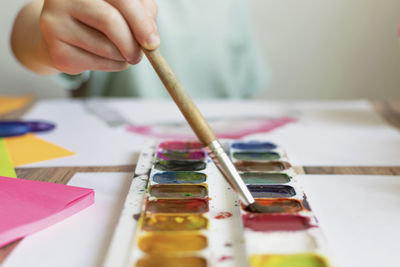 Cropped hand of boy holding paintbrush over palette while painting at classroom