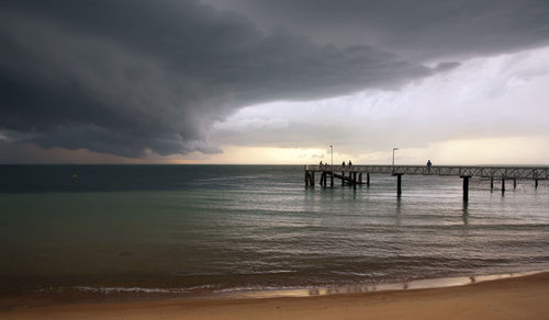 Huge black storm clouds gather as silhouetted people fish off a pier