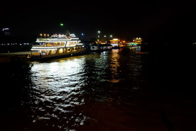 Illuminated boats in river against sky at night