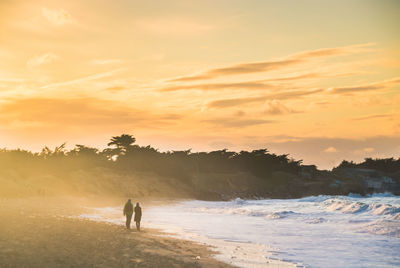 Couple on beach against sky during sunset