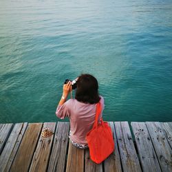 Rear view of man photographing while sitting on pier