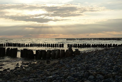 Wooden posts on beach against sky during sunset