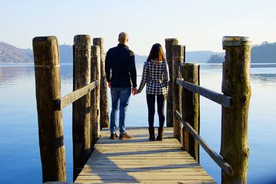 Rear view of couple standing at pier in lake against sky